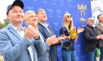 Olimpiada Seniorów Nieporęt 2026 - rozpoczęcie imprezy - wciągnięcie flagi olimpijskiej na maszt obserwują włodarze zaproszonych gmin